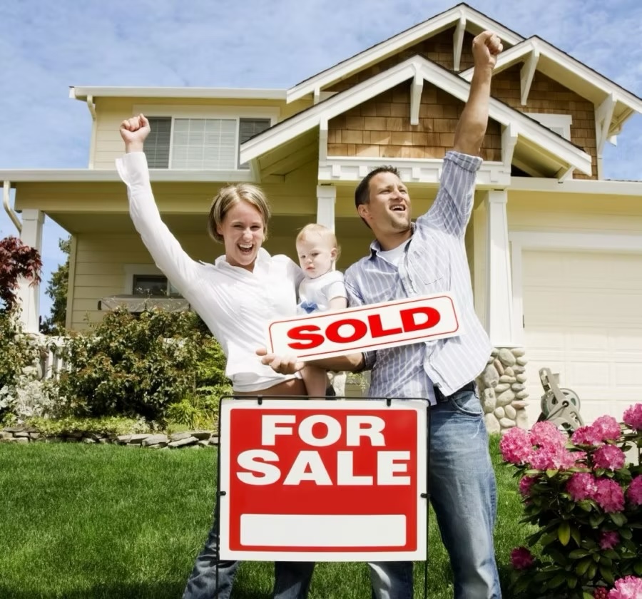 family celebrating behind for sale sign, holding sold sign